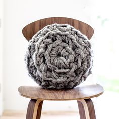 a gray and white knitted object sitting on top of a wooden chair in front of a window