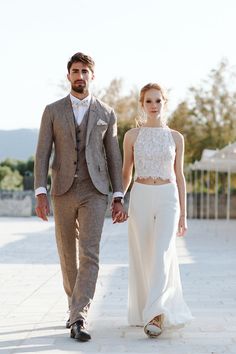 a man and woman are walking down the street holding hands while dressed in formal clothing