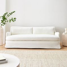 a white couch sitting on top of a wooden floor next to a vase filled with green plants