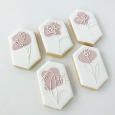 four decorated cookies sitting on top of a white table next to each other with pink frosting