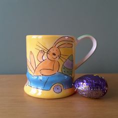 a coffee cup with a bunny on it next to an easter chocolate egg in the shape of a car