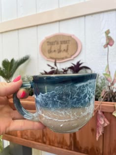 a hand holding a blue and white coffee cup with waves on the inside, in front of a potted plant