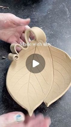 two hands are holding an object that looks like a leaf and has the words made with clay on it