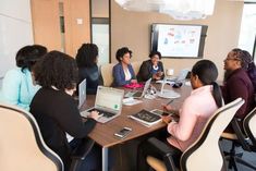 a group of people sitting around a table with laptops and papers in front of them