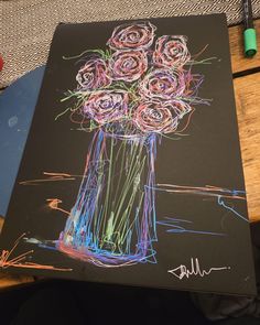 a drawing of flowers in a vase on a black paper with colored crayons