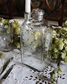 a glass bottle with flowers in it sitting on a table next to some silverware