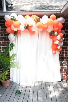 an orange and white balloon arch with palm leaves