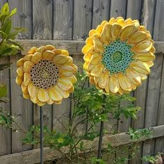 two yellow sunflowers sitting on top of a planter in front of a fence