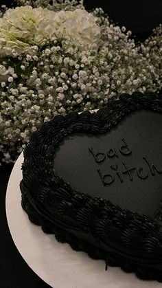 a black heart shaped cake sitting on top of a white plate with flowers in the background