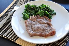 a white plate topped with meat and veggies on top of a place mat