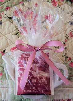 a pink ribbon wrapped in clear plastic on top of a quilted bed with a cup and saucer