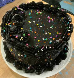 a large chocolate cake with sprinkles on a white plate and wooden table