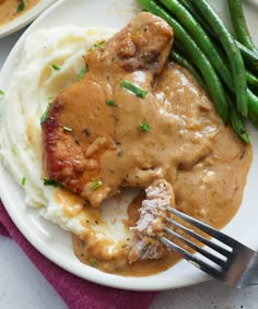 a white plate topped with meat and gravy covered in gravy next to green beans