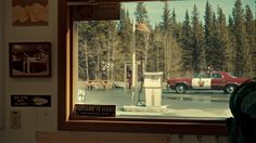 a red car is parked in front of a gas station with trees outside the window