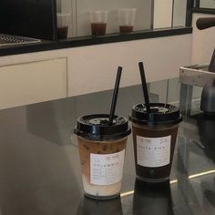 two coffee cups sitting on top of a counter next to each other with black straws in them