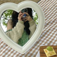 a woman taking a selfie in front of a heart shaped mirror on a picnic table