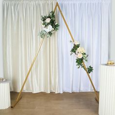 a wedding arch with flowers and greenery on it in front of a white curtain