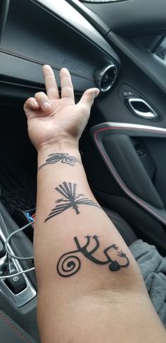 a person with a tattoo on their arm in a car holding up the steering wheel