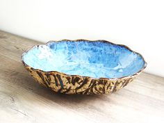 a blue and brown bowl sitting on top of a wooden table next to a white wall