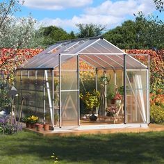 a small greenhouse in the middle of a garden with flowers and plants growing inside it