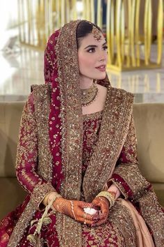 a woman sitting on top of a couch wearing a red and gold wedding dress with her hands in her pockets