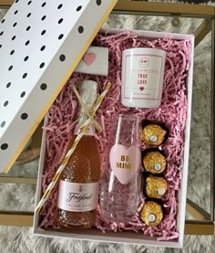 a pink box with two bottles of booze and some chocolates in it on a white carpet