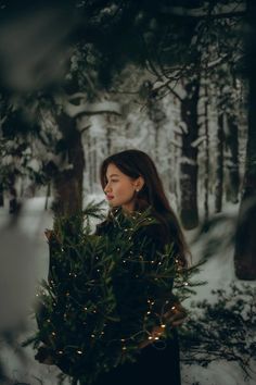 a woman standing in the snow holding a christmas tree with lights on it's branches