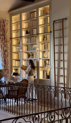 a woman standing in front of a book shelf filled with books next to a window