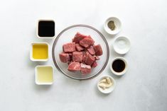 raw meat and spices on a white table with ingredients for the recipe in small bowls