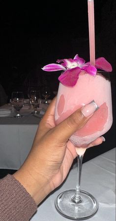 a person holding up a pink drink in front of a table with white linens