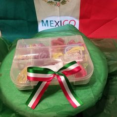 a plastic container filled with food on top of a green cloth covered table next to a mexican flag