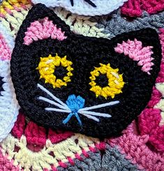 a crocheted black cat with yellow eyes laying on top of a pink and white blanket