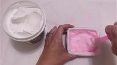 a person is spreading pink paste in a container on a table next to a cup of ice cream