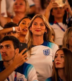 a group of people sitting next to each other at a soccer game with one woman holding a cell phone