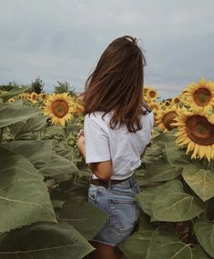 a woman standing in the middle of a sunflower field with her back to the camera