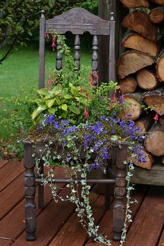 a wooden chair with flowers in it sitting on a deck next to a pile of logs