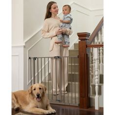 a woman holding a baby in her arms while standing next to a dog on the floor