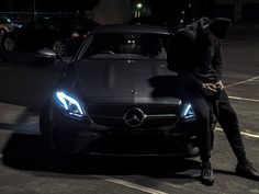 a man sitting on the hood of a black car in a parking lot at night