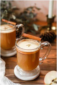 two mugs filled with hot chocolate and cinnamon on top of a wooden table next to an apple