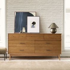 a white brick wall in a living room next to a wooden dresser with two lamps on top