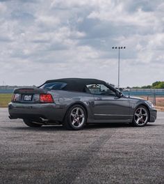 a gray sports car parked on top of a parking lot next to an empty field