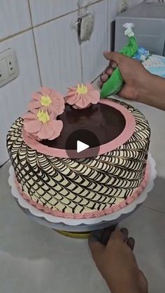 someone is decorating a cake with pink flowers on the top and brown icing