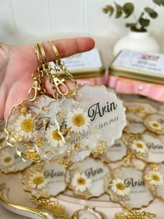 a person holding a small white flower key chain on top of a plate with other items in the background