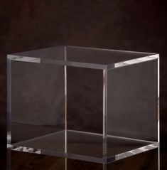 an empty glass box sitting on top of a wooden table in front of a dark background