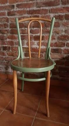 a green wooden chair sitting on top of a tile floor next to a brick wall