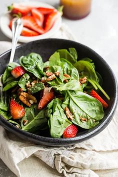 a bowl filled with spinach and strawberries on top of a white table cloth