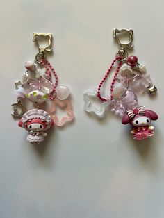 two pairs of earrings with charms attached to them on a white surface, one is pink and the other is silver