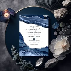 a blue and white wedding card on top of a black plate with flowers next to it