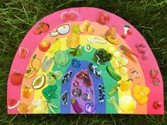 a rainbow shaped paper plate with fruit and vegetables on it in the middle of grass