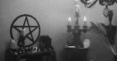 a black and white photo of a living room with candles on the table in front of a pentagram